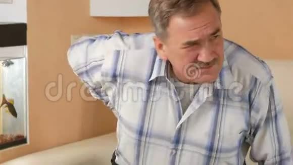 有胡子的老人因为背痛不能下沙发他用双手抓住腰部视频的预览图