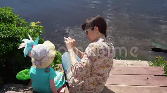 妈妈和小女儿坐在湖边的码头上视频的预览图