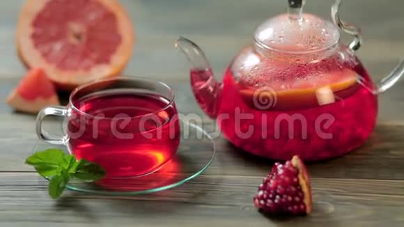 玻璃茶壶和一杯带葡萄石榴薄荷的红茶放在棕色的木桌上视频的预览图