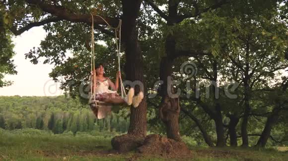 孩子们在公园的秋千上晒太阳年轻女孩在橡木树枝上的绳子上摆动少女喜欢飞行视频的预览图