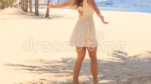 穿白色连衣裙的苗条女孩双手放在沙滩上摇摆视频的预览图