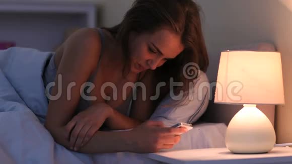躺在床上在智能手机上发短信笑容满面的黑发女人视频的预览图
