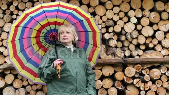 穿着绿色雨衣带着伞站在木头旁边的女人视频的预览图