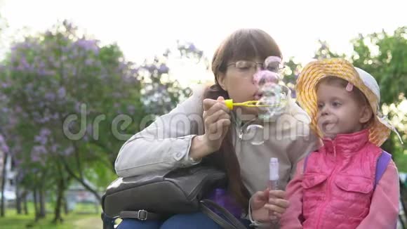 阳光明媚的春天一家人在盛开的紫丁香公园里吹着肥皂泡视频的预览图