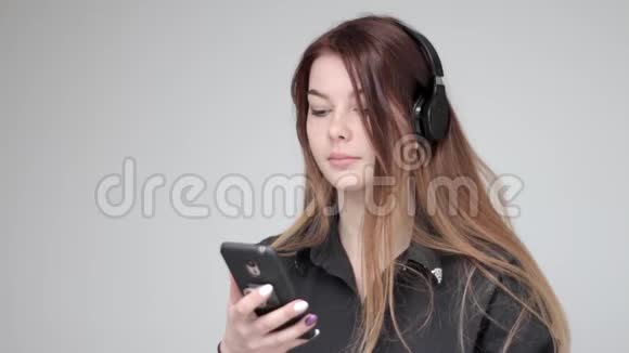 漂亮的年轻快乐的女孩听音乐耳机浅色背景视频的预览图