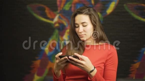 年轻漂亮的女孩穿着红色连衣裙使用智能手机在房间里慢动作视频的预览图