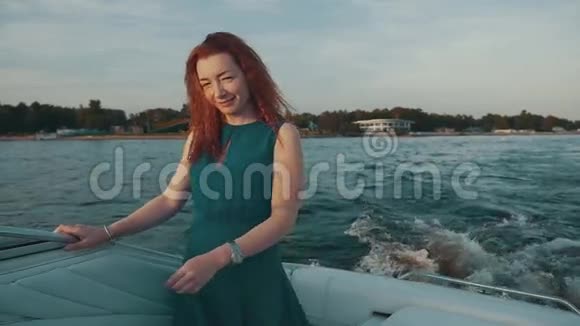 快乐的红发女孩穿着绿松石的裙子在摩托艇上抚摸头发很有趣微笑视频的预览图