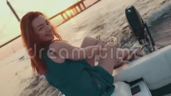穿着绿松石色连衣裙的小女孩坐在摩托艇的边上享受日落视频的预览图