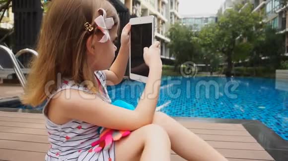 小女孩在游泳池附近玩平板电脑视频的预览图