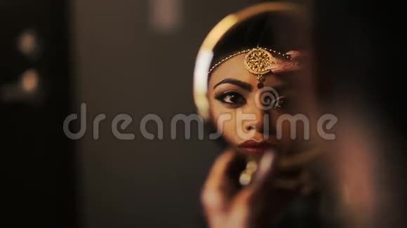 美丽的印度新娘拿着一面圆镜子而女人则画着她的嘴唇视频的预览图