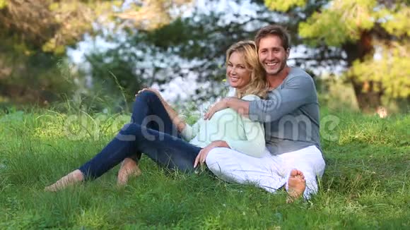 美丽的金发情侣坐在绿色的草地上视频的预览图