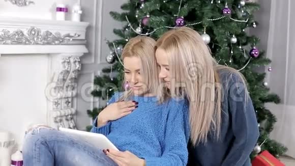 两个金发女孩正盯着圣诞树附近的平板电脑视频的预览图