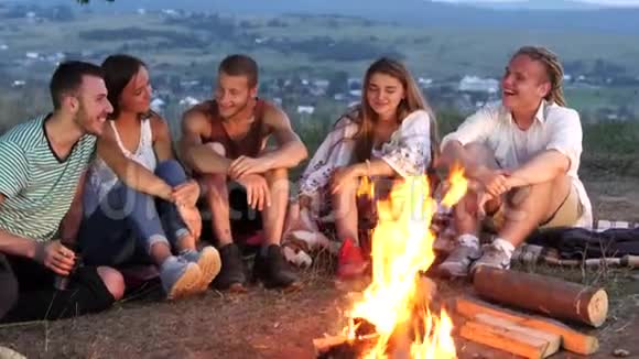 一群朋友坐在篝火旁喝着热饮料和交谈视频的预览图