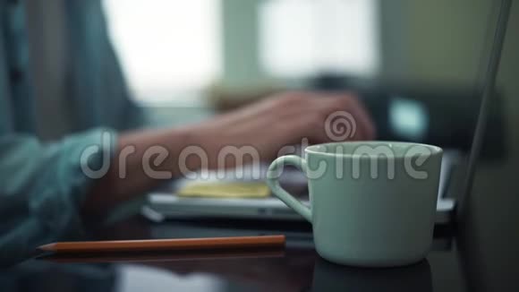 男性手从桌子上拿起白色的杯子在办公室用笔记本电脑的人视频的预览图