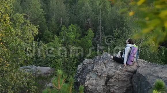 年轻女子背包客坐在大岩石上放松日出视频的预览图