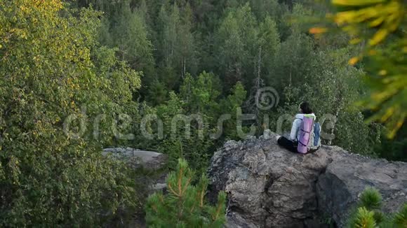 年轻女子背包客坐在大岩石上放松日出视频的预览图