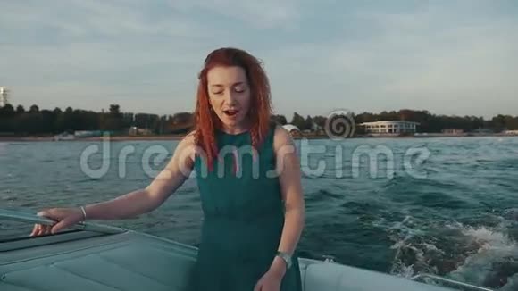 快乐的红发女孩穿着绿松石衣服在摩托艇上跳舞夏季视频的预览图