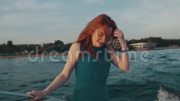 快乐的红发女孩穿着绿松石衣服在摩托艇上笑吐舌头乐趣视频的预览图