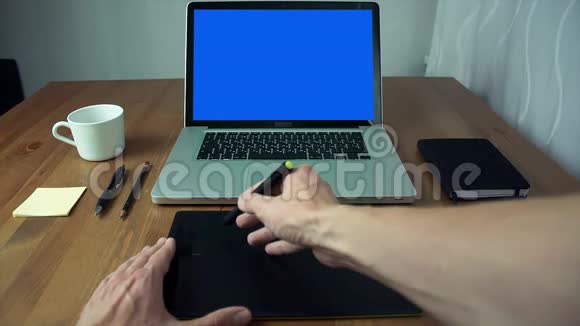 在白色桌子上使用带有绿色屏幕的图形标签和笔记本电脑查看男性手视频的预览图