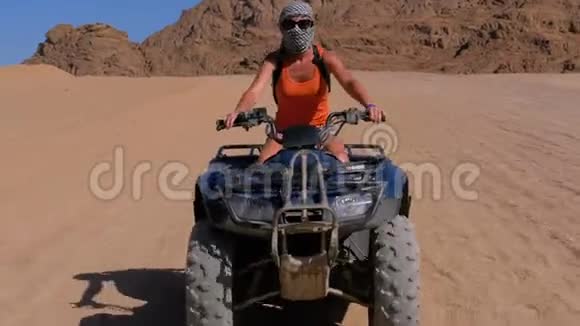 骑着四轮自行车的女孩骑着自行车穿越埃及沙漠以山脉为背景视频的预览图