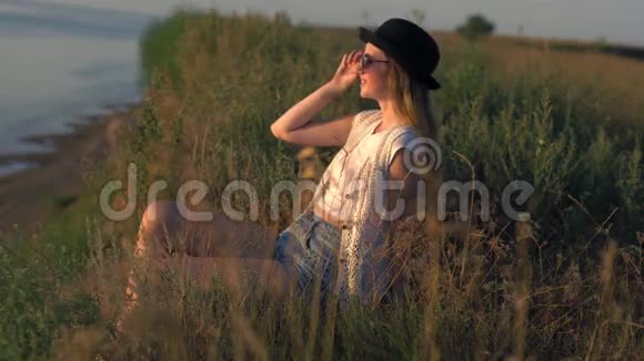 戴墨镜的年轻女子坐在悬崖边享受大自然视频的预览图