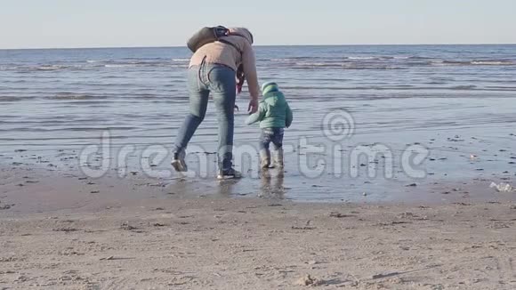 妈妈带着一个小孩沿着春天的海滩散步视频的预览图