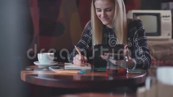 现代女孩在咖啡馆喝茶使用平板电脑和写在笔记本视频的预览图