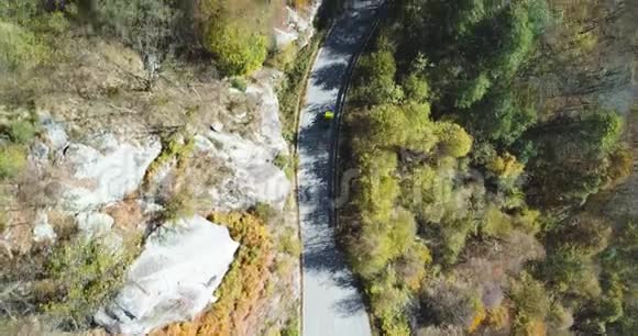 空中俯视黄色老式汽车行驶在五彩缤纷的秋天森林的道路上秋天的橙色绿色的树视频的预览图