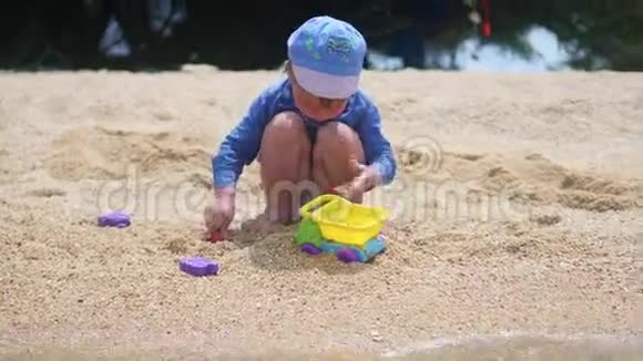 一个孩子在阳光明媚的热天在海滩上玩沙子和玩具视频的预览图