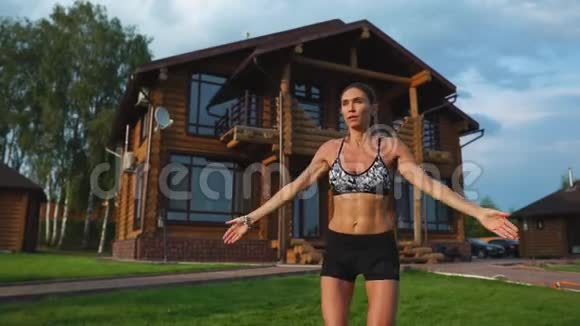 在草坪上的房子背景上穿着运动服的苗条美丽的女人为有氧训练和肥胖表演跳跃视频的预览图