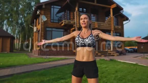在草坪上的房子背景上穿着运动服的苗条美丽的女人为有氧训练和肥胖表演跳跃视频的预览图
