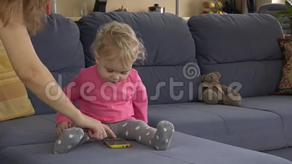 妈妈帮可爱的宝贝女儿用智能手机坐在沙发上视频的预览图