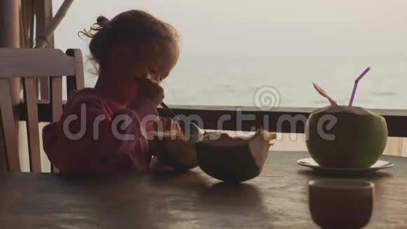 小可爱的女孩在咖啡馆用勺子吃椰子海景慢镜头视频的预览图