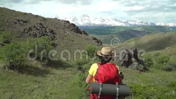那个带着红色背包的旅行者的女人站在山上看着雪山视频的预览图