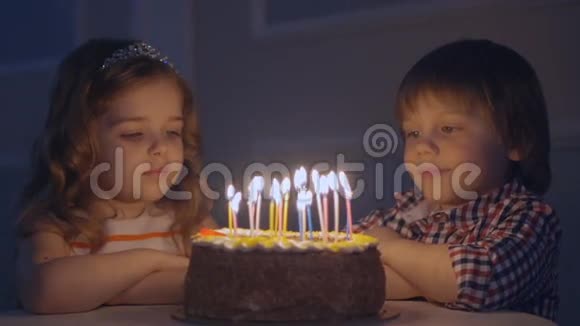 一个小男孩和一个女孩在一个庆祝蛋糕上看许愿然后在蛋糕上吹蜡烛视频的预览图