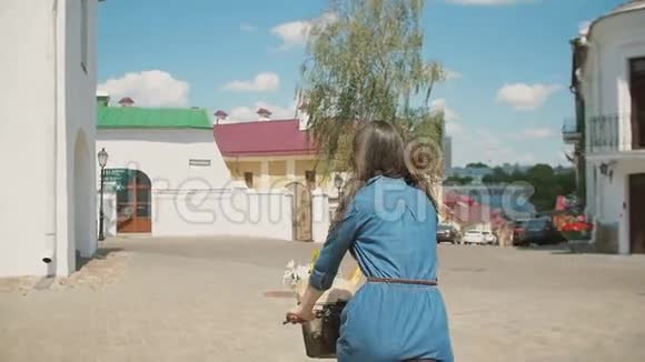 街上一个穿着蓝色裙子骑着花篮的自行车的女孩的后景慢的稳定的镜头视频的预览图