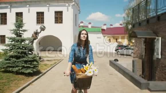 快乐美丽的女孩骑着自行车花和法国面包放在篮子里微笑着慢着稳健的射击视频的预览图