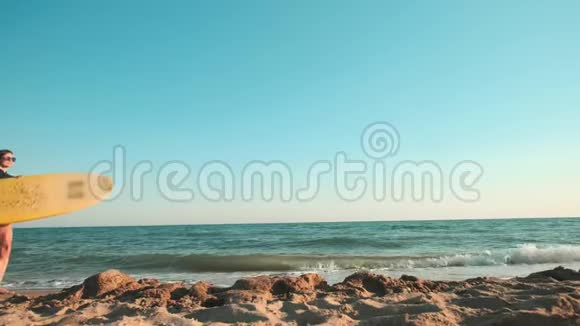 美丽苗条的女孩走在海滩上拿着冲浪板傍晚日落时跑步穿着泳装视频的预览图