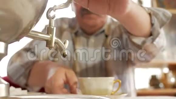 一对老夫妇用一个老式的俄罗斯水壶萨莫瓦尔准备茶一个留胡子的男人给妻子倒茶视频的预览图