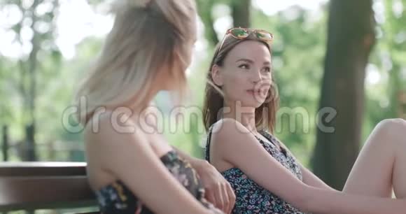 两个年轻女孩坐在公园的长凳上享受夏天和聊天视频的预览图