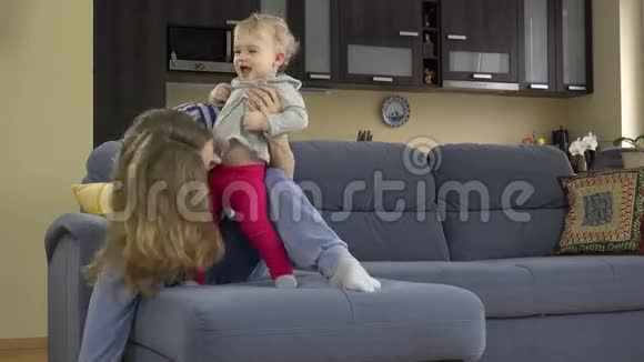 美丽的女人搔着蹒跚的孩子的肚子坐在沙发上视频的预览图