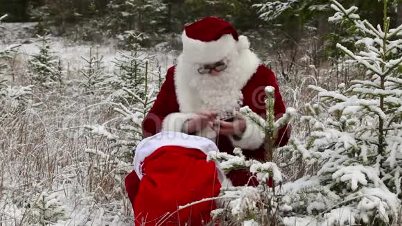 圣诞老人和平板电脑在雪林的礼品袋附近视频的预览图