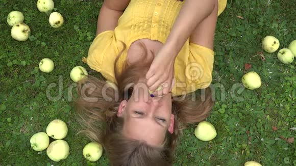 美丽微笑的年轻女子躺在草地上咬着苹果水果4K视频的预览图