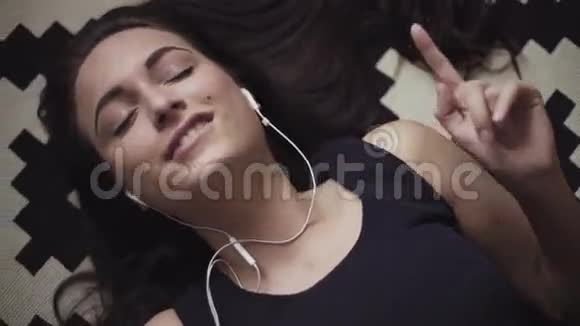 全景画面显示年轻女性如何躺在地板上用耳机听并移动手机上的音乐视频的预览图