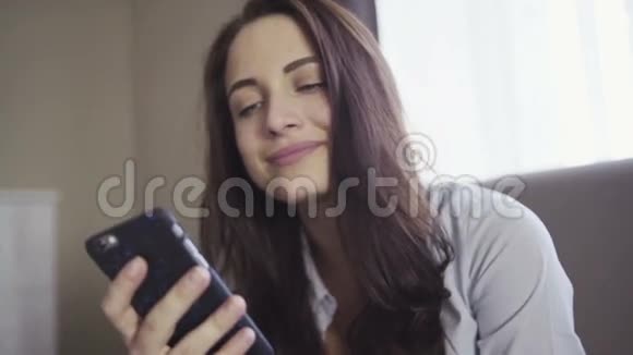 慢动作镜头显示黑发女孩是如何坐在客厅的沙发上看着智能手机屏幕视频的预览图