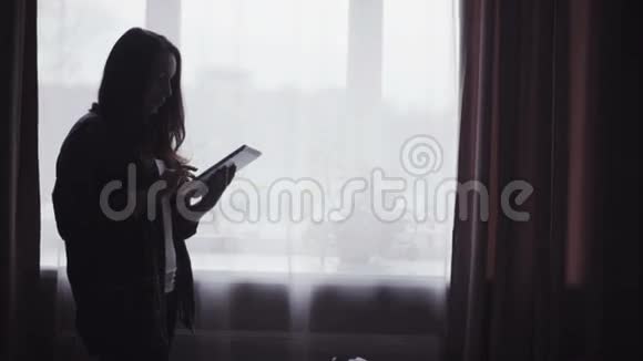 慢镜头与一个年轻的长发妇女剪影谁正在使用移动设备室内视频的预览图