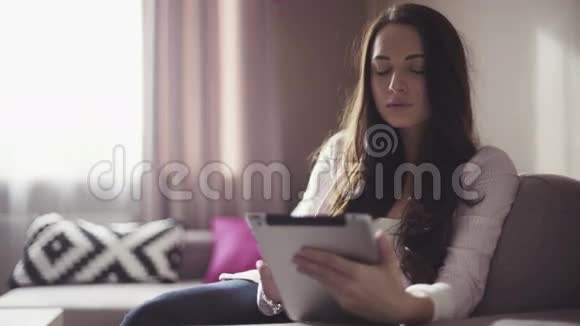 20多岁的英俊女性坐在客厅里使用她的移动设备视频的预览图