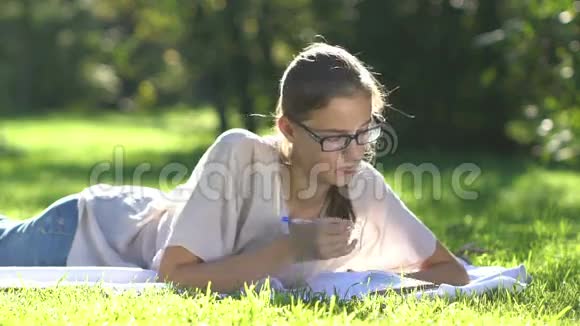 草地上年轻漂亮的女孩写笔记本视频的预览图