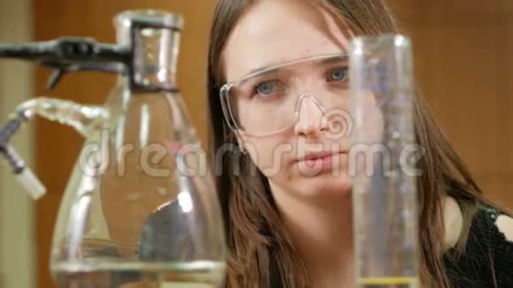 年轻的女学生从事化学工作并在大学里写出结果安全眼镜无外袍烧杯和视频的预览图