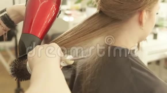发型师在美容院理发后烘干女性头发用吹风机和吹风机将理发师的长头发定型视频的预览图
